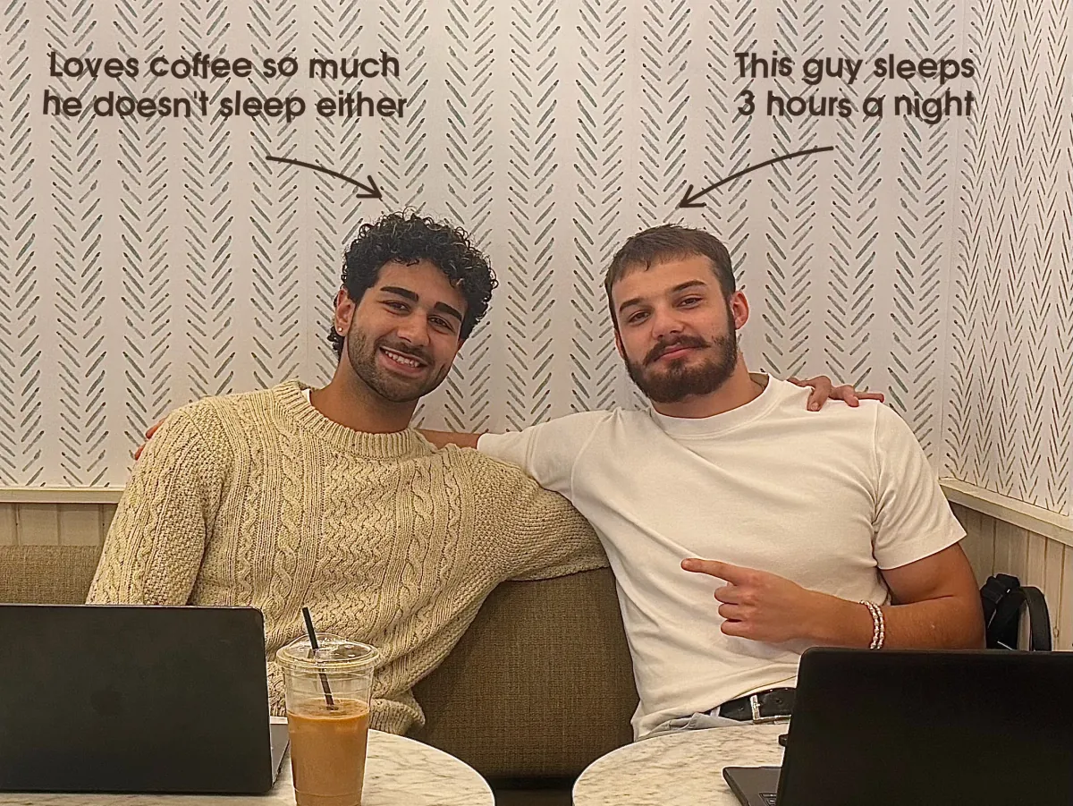 George and Keyon, the two founders of kava, sit side by side at a café table with their laptops and an iced coffee. Hand-written notes point at them: Loves coffee so much he doesn't sleep either. This guy sleeps 3 hours a night.
